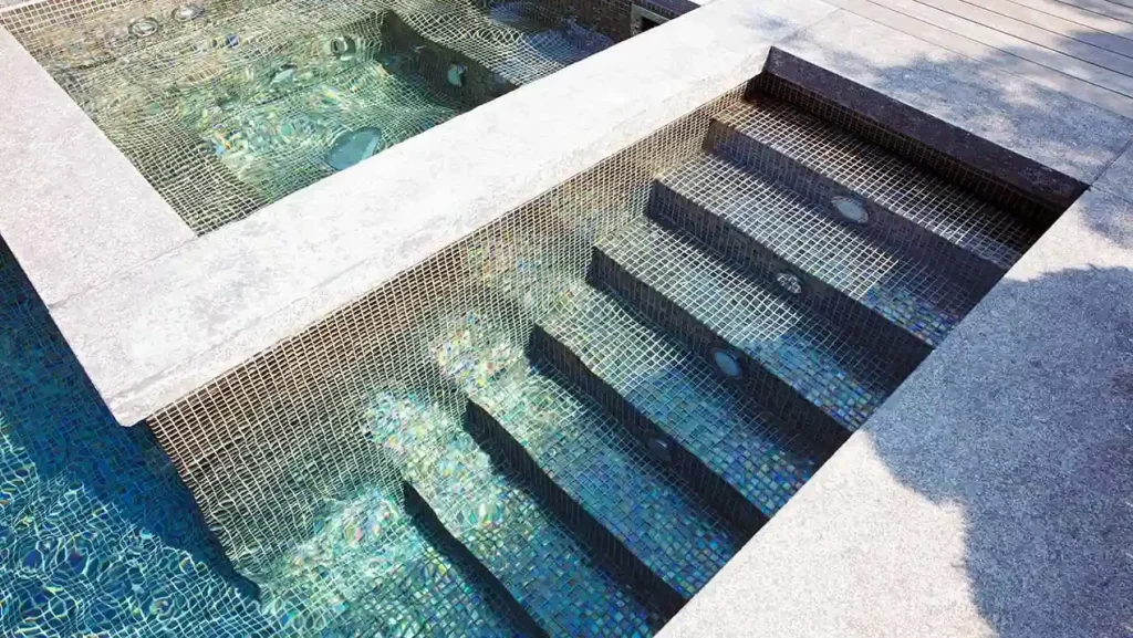 Detailansicht einer Treppe aus Mosaikfliesen, die in einen modernen Pool mit Whirlpool-Bereich führt.