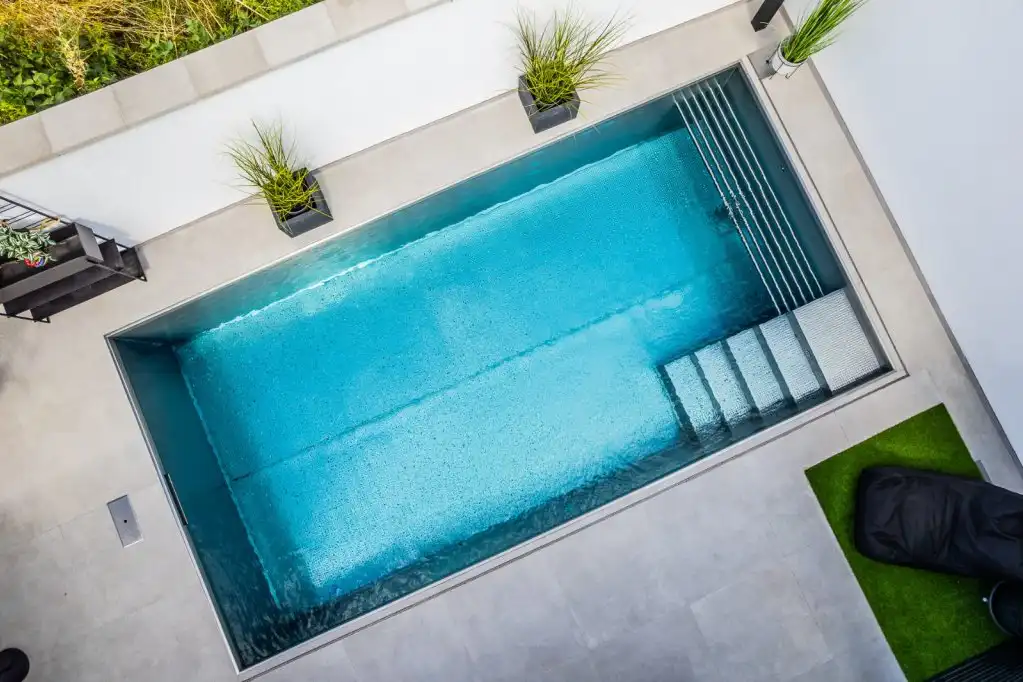 Moderner rechteckiger Edelstahlpool in Würzburg mit Treppe und hellem Fliesenrand in einem kleinen Innenhof.