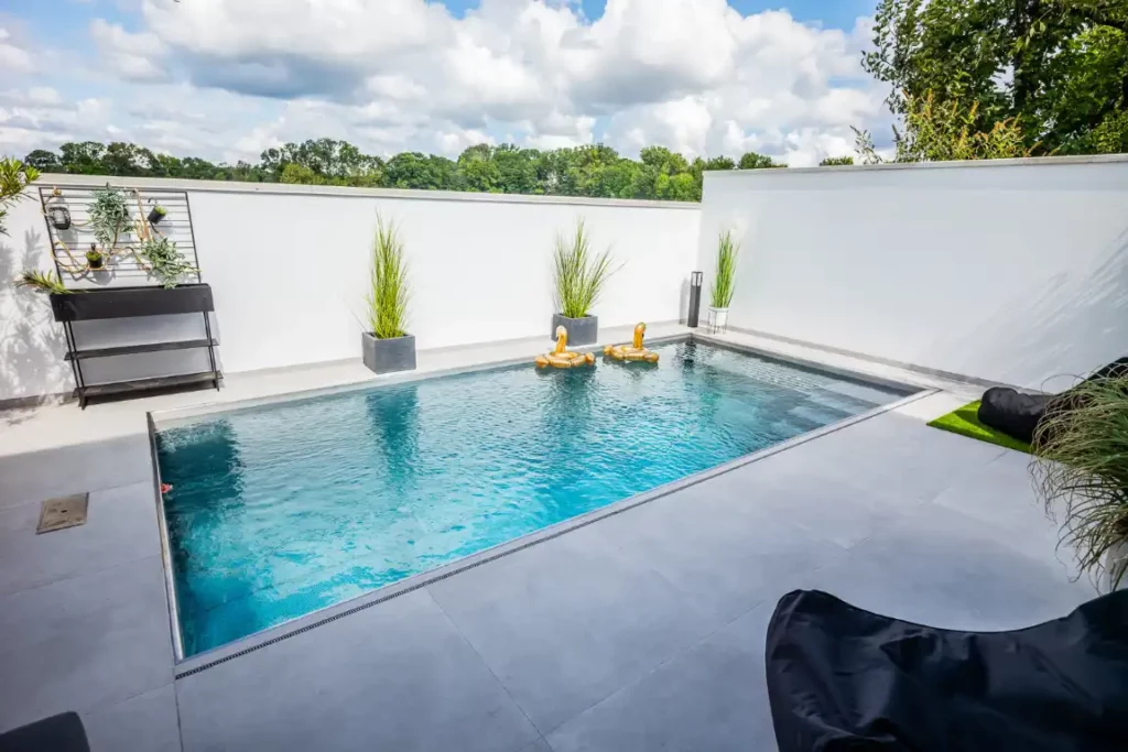 Rechteckiger Edelstahlpool in Würzburg in einem modernen Innenhof mit weißen Wänden und Pflanzen in grauen Töpfen.