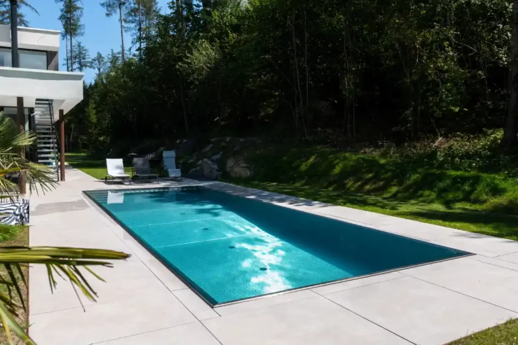 Terrasse mit Liegestühlen, angrenzendem Waldstück und modernem Edelstahlpool in der Nähe von Würzburg.