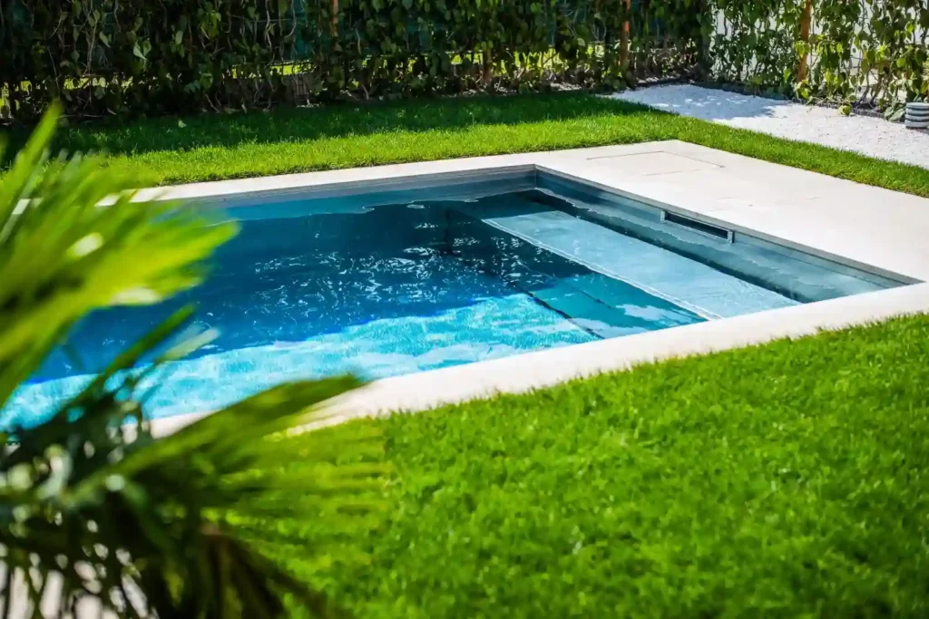 Moderner rechteckiger Gartenpool mit klarem Wasser, umgeben von dichtem Rasen und hellen Steinplatten.