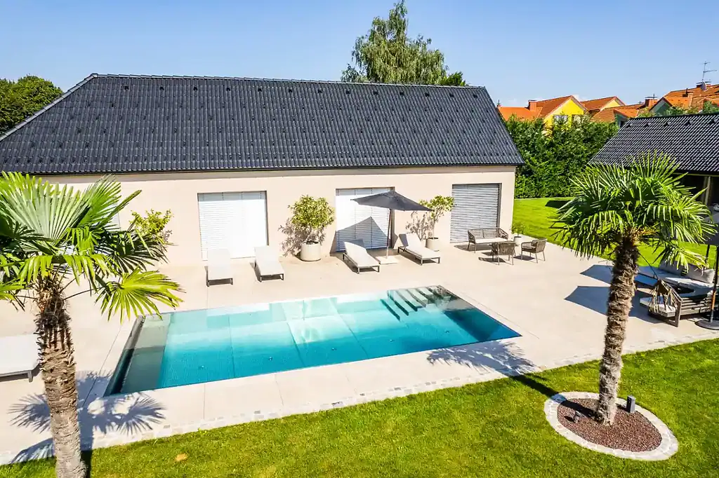 Edelstahlpool mit einer großen Terrasse mit mehreren Liegestühlen und Palmen in einem Garten in einem Ort in Mainfranken.