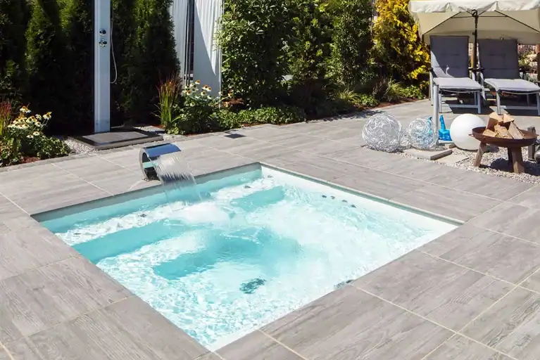 Mini-Pool mit Wasserfall, umgeben von einer Terrasse mit grauen Steinplatten in einem Garten in Würzburg.