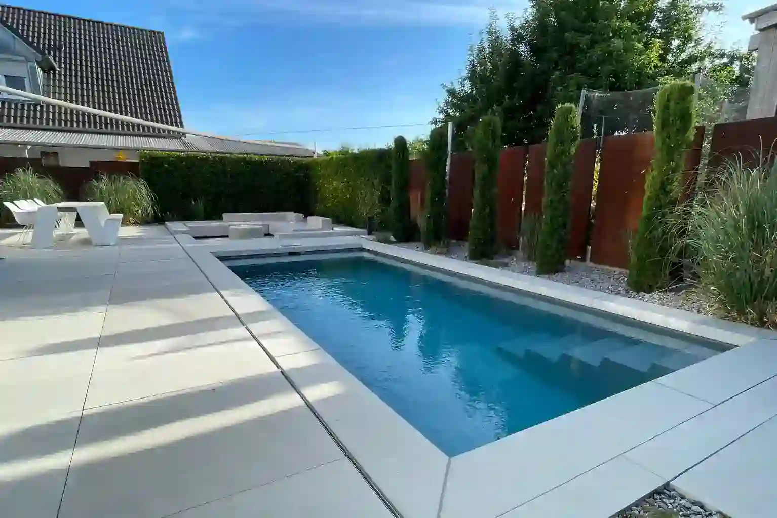 Moderner Skimmerpool in Würzburg mit Lounge, großer Terrasse und Hecke im Hintergrund.