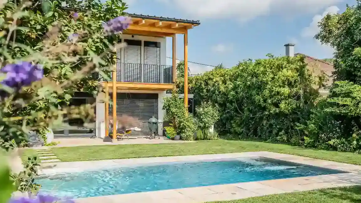Rechteckiger Edelstahlpool von Papajewski und AQASTEEL vor einem modernen Haus mit Holzveranda und grüner Bepflanzung.