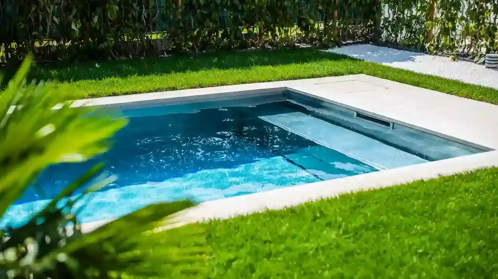 Moderner rechteckiger Gartenpool mit klarem Wasser, umgeben von dichtem Rasen und hellen Steinplatten.