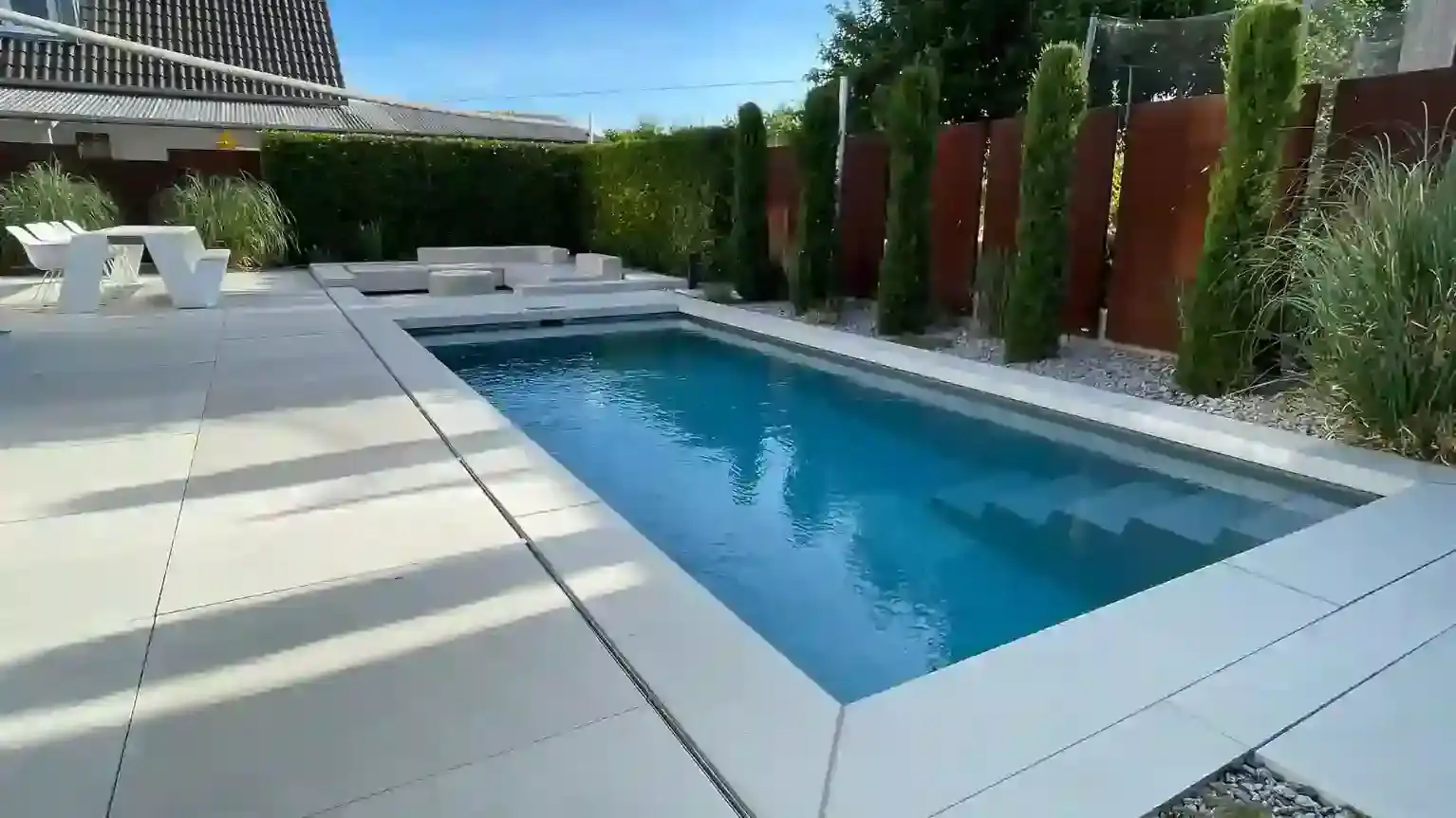 Moderner Skimmerpool in Würzburg mit Lounge, großer Terrasse und Hecke im Hintergrund.