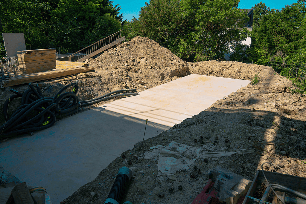 Poolbau Baustelle mit vorbereiteter Baugrube und Betonfundament im Garten