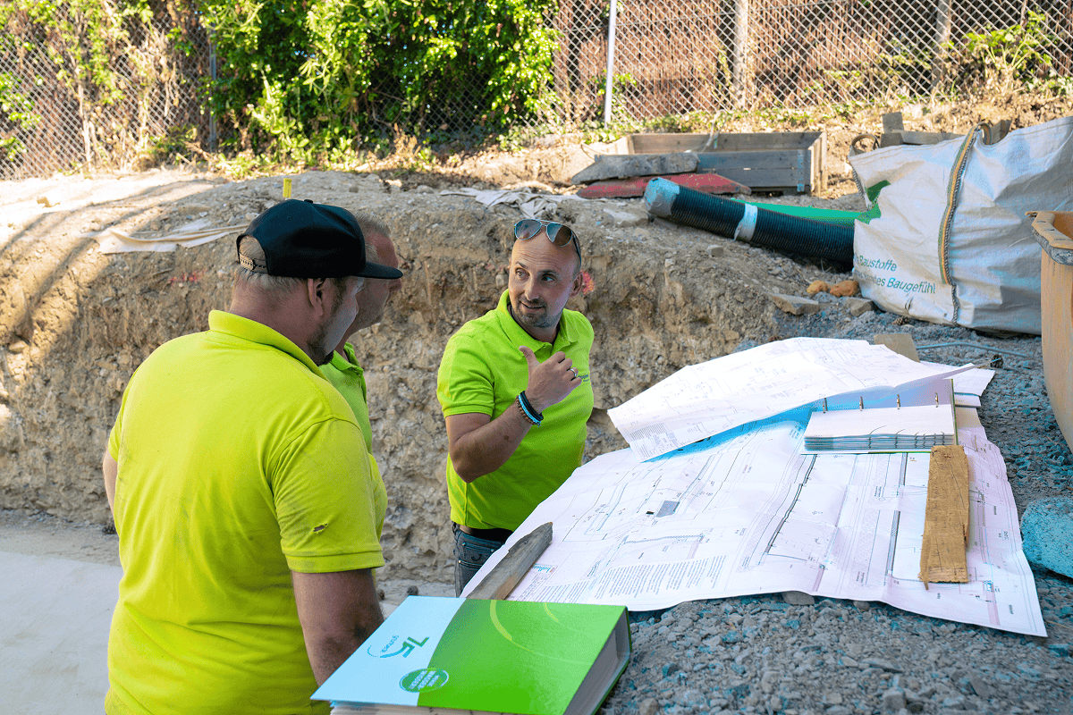 Drei Poolbauer in grünen Shirts besprechen Baupläne auf der Baustelle