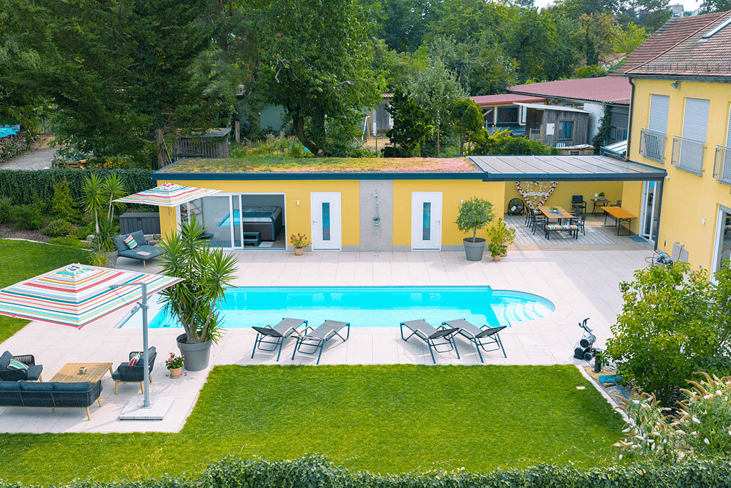 Poolbau Referenz mit gepflegte Gartenanlage mit Pool und Loungebereich vor einem gelben Landhaus