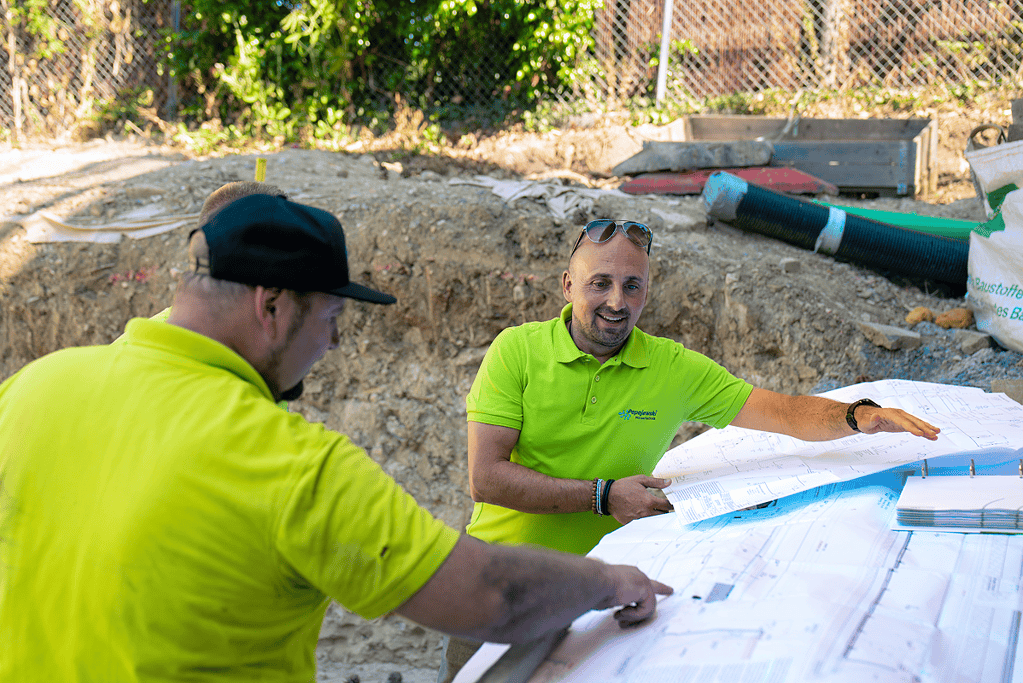 Drei Poolbauer besprechen Baupläne auf der Baustelle neben der Baugrube