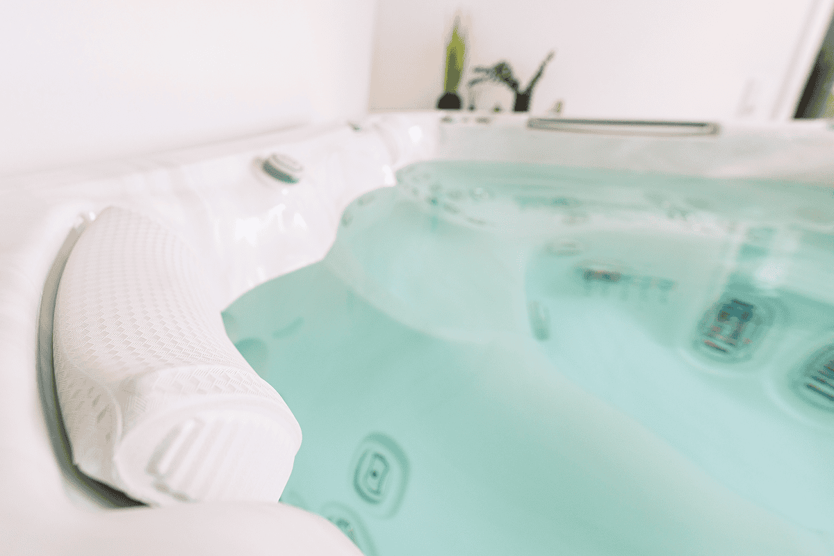 Weißer Whirlpool mit gepolsterter Kopfstütze und türkisfarbenem Wasser im Innenbereich