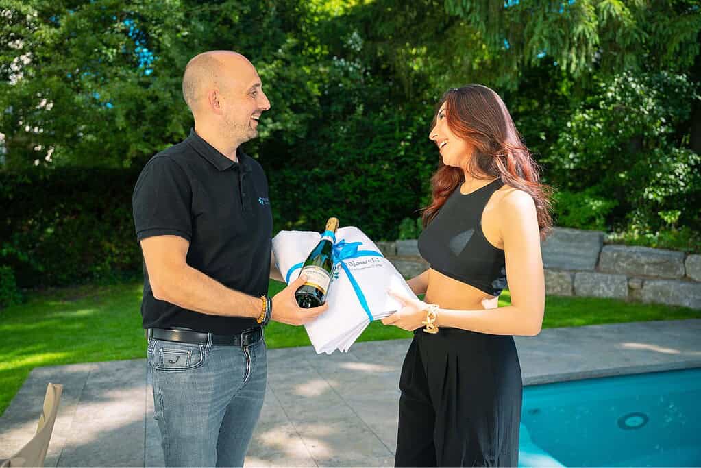 Stephan Papajewski überreicht der Kundin zu ihrem neuen Minipool Sekt und ein Papajewski-Handtuch.