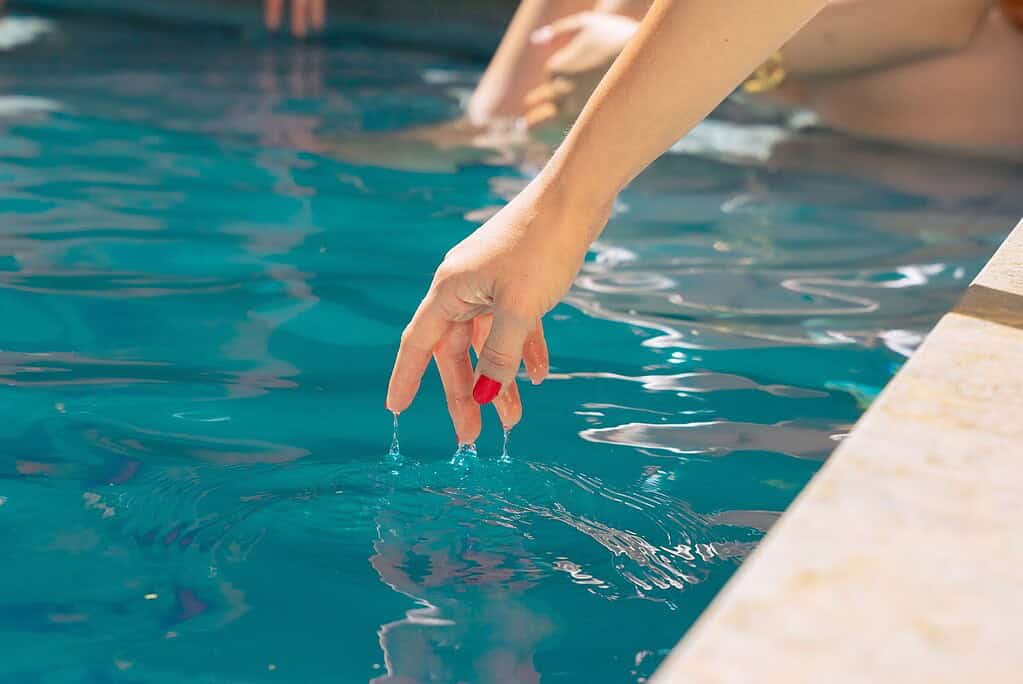 Frau testet mit ihren Fingern, wie warm das Wasser in ihrem Minipool ist.